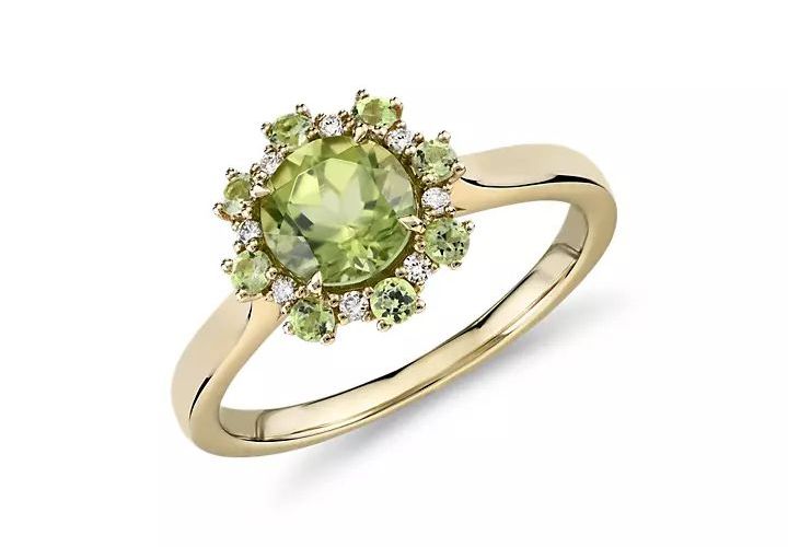 An August birthstone ring of peridot round-cut center gemstone surrounded by diamond and more peridots as floral petals and set in yellow gold